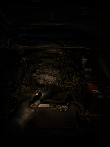 Squinting into a dark engine bay, flashlight in mouth